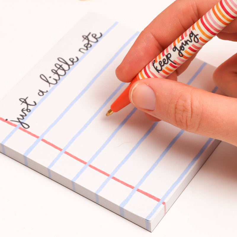 Hand holding a pen with striped design over a lined memo pad