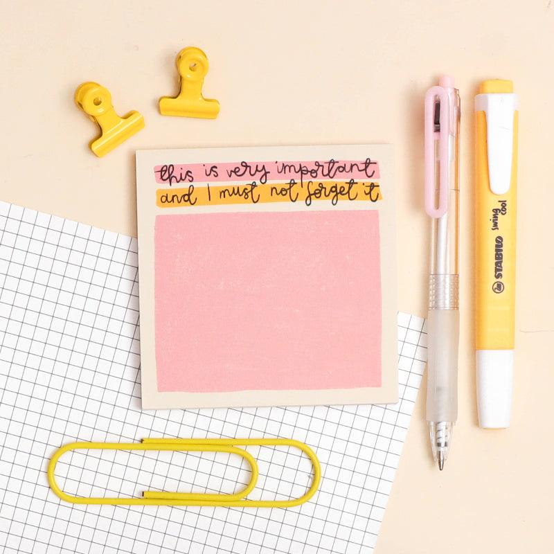 Pink sticky note with text, yellow pen, and office supplies on a grid background