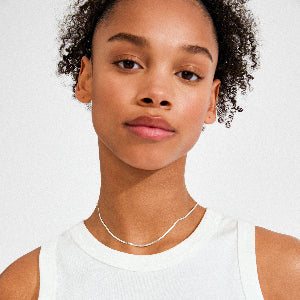 Woman wearing a white tank top and necklace against a plain background