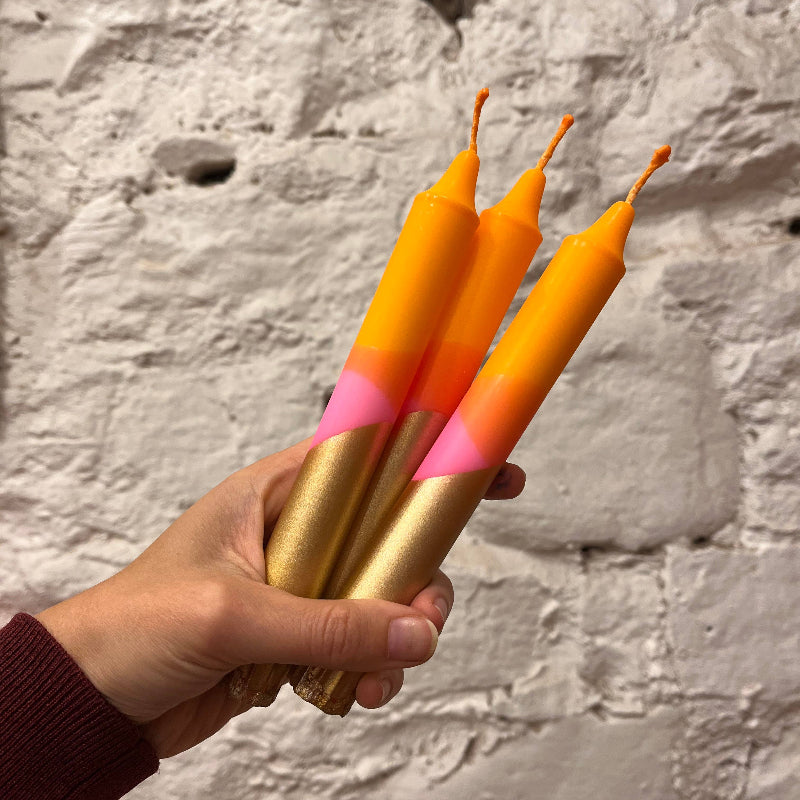 Hand holding three colorful candles against a stone wall background