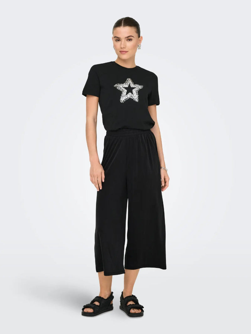 Woman wearing a black t-shirt with a star design and black wide-leg pants on a white background