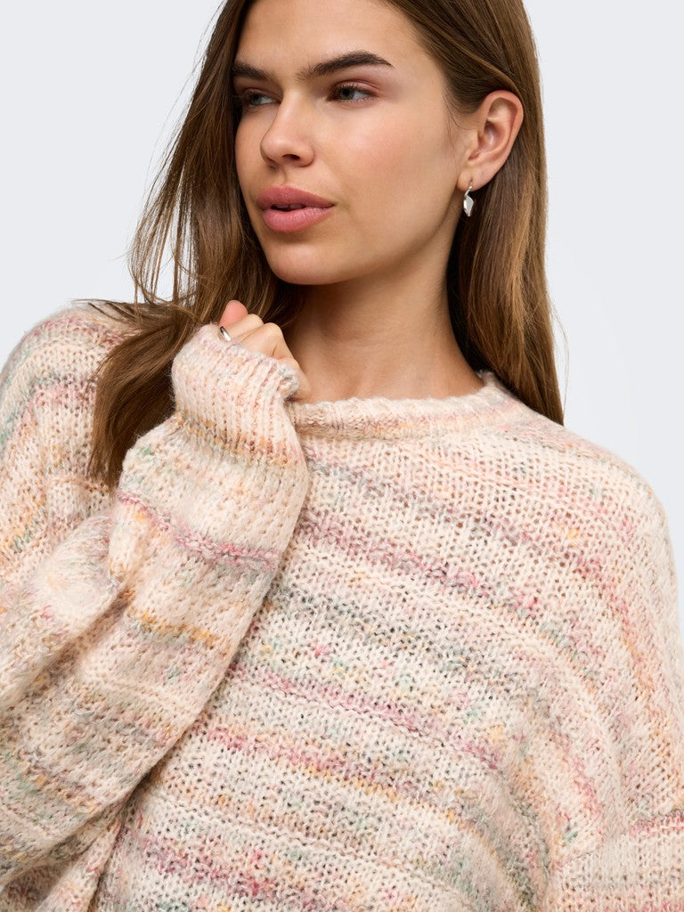 A close-up of a woman wearing a chunky knit crewneck sweater with a marled pastel pattern of pink, orange, and yellow on a cream base, set against a plain light gray background.