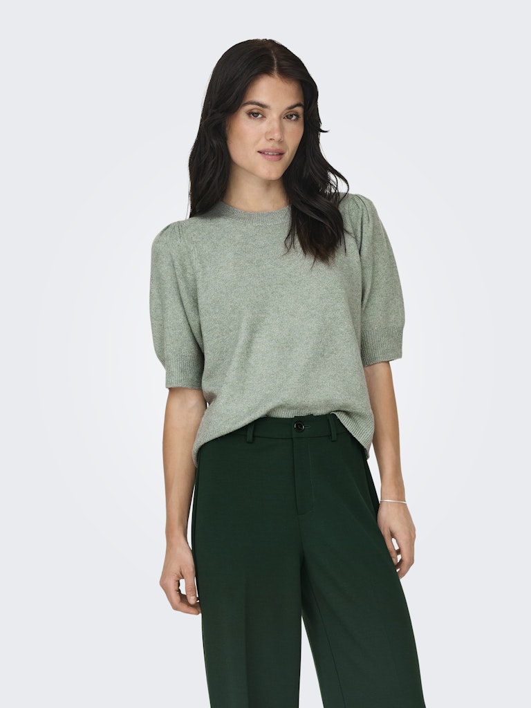 Woman wearing a green sweater and dark green pants on a white background