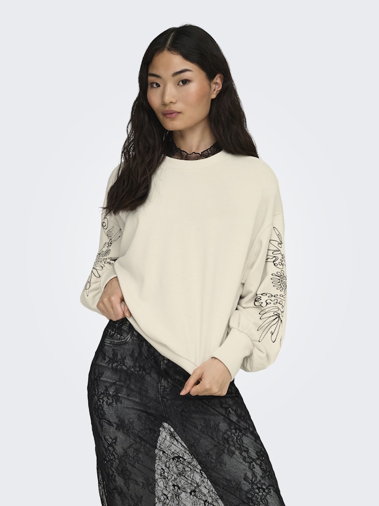 Woman wearing a cream Only Brooke sweater with lace sleeves and black lace pants on a white background