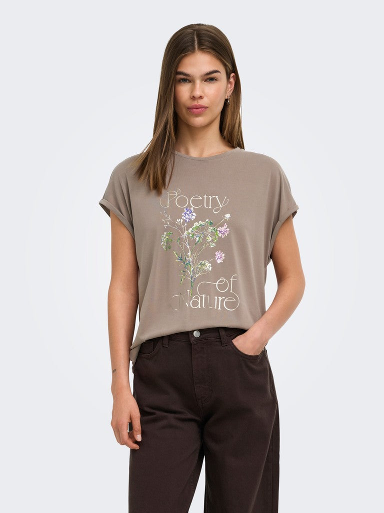A woman modeling a taupe short-sleeve graphic t-shirt with a floral design and the words 'Poetry of Nature' printed on the front, paired with dark brown pants, against a light gray background.