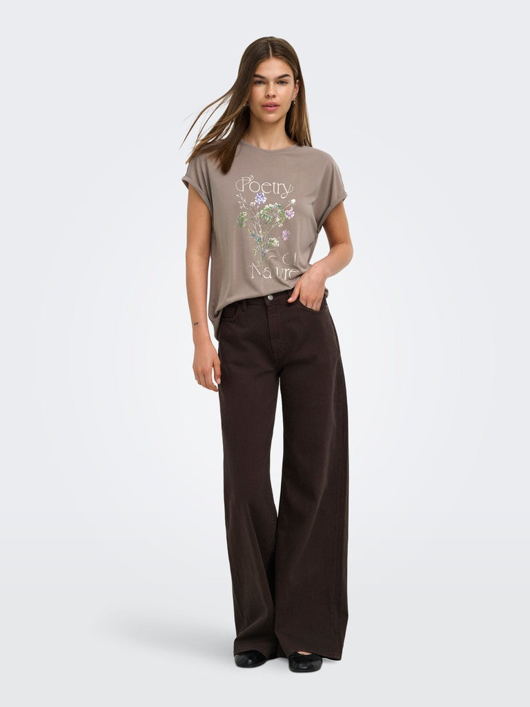 A woman modeling a taupe graphic t-shirt with a floral print and the word 'Poem' on the front, paired with dark brown wide-leg trousers, against a light gray studio background.