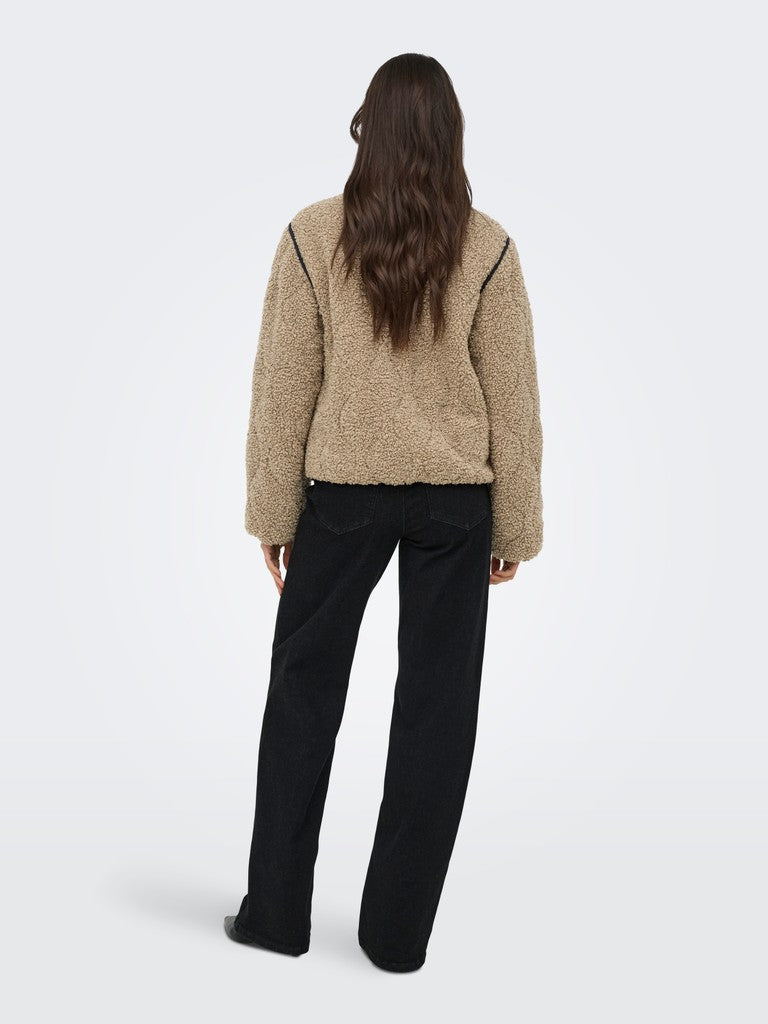 A woman viewed from the back wearing a beige sherpa fleece cropped jacket with black shoulder piping and black wide-leg trousers, set against a light gray studio background.