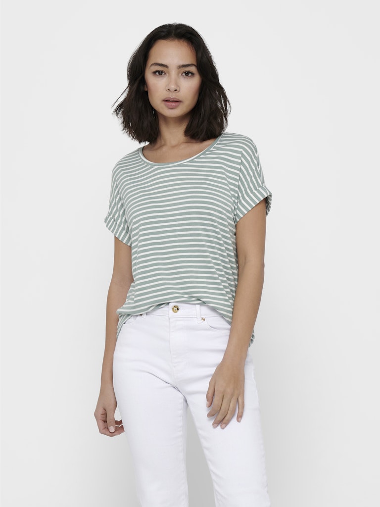 Woman wearing a green and white striped shirt and white pants on a plain background