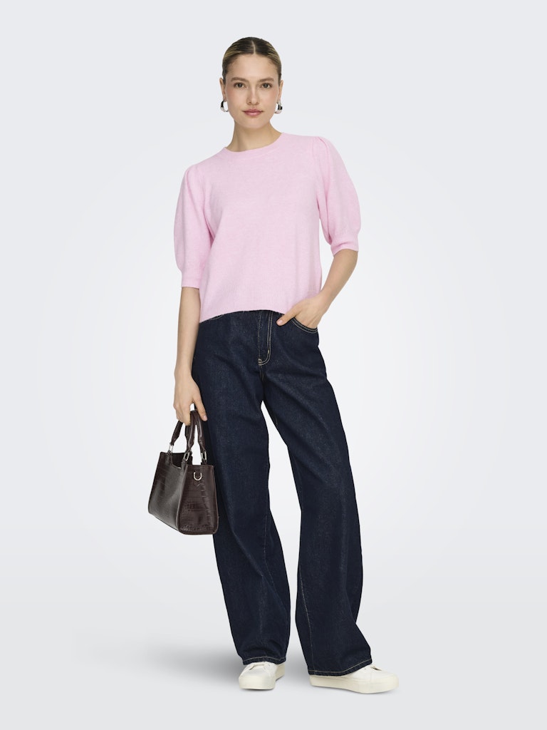 Woman wearing a pink sweater and dark jeans with a brown handbag on a white background
