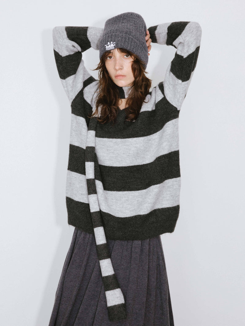 Person wearing a black and gray striped sweater and hat on a white background