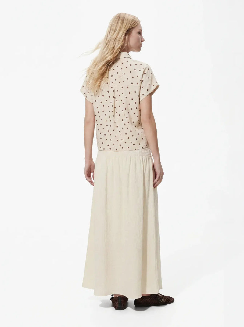 Woman wearing a polka dot blouse and long cream skirt on a white background
