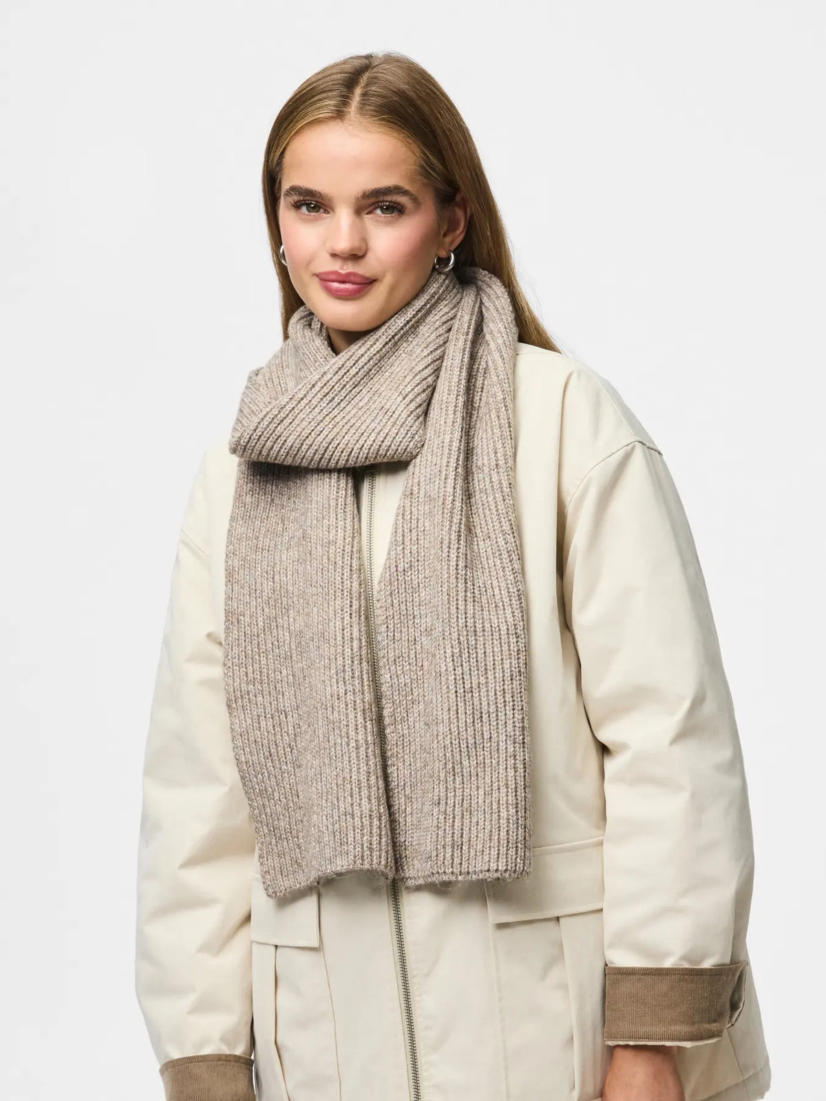 Woman wearing a beige scarf and cream coat on a white background
