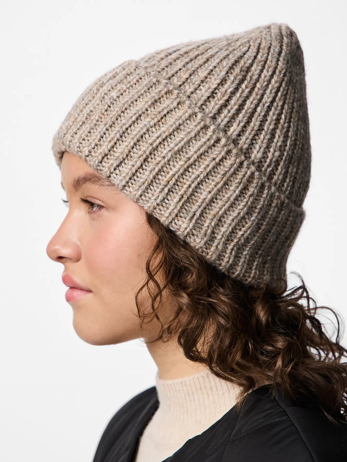 Person wearing a beige knit beanie on a white background