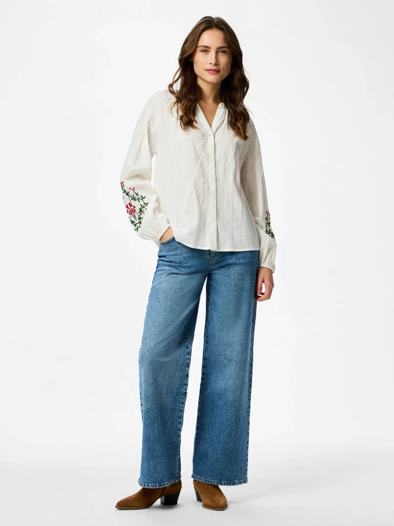 Woman wearing a white blouse with floral embroidery and blue jeans on a white background