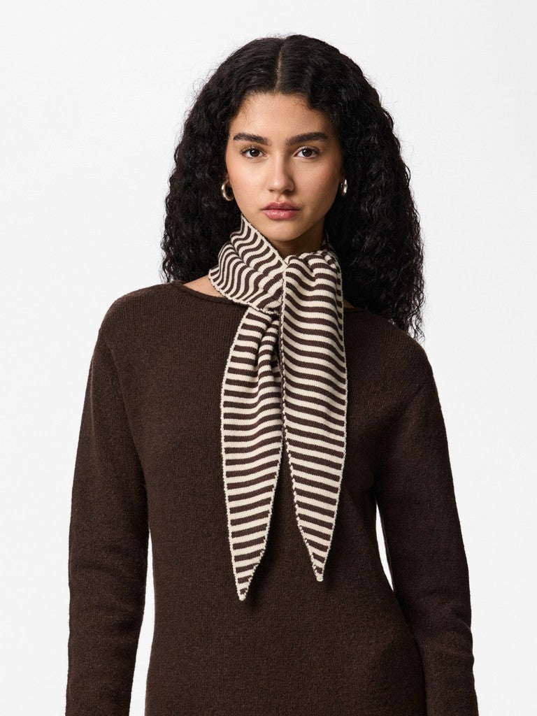 A woman with long, curly dark hair is shown from the chest up wearing a dark brown knit sweater and a striped scarf with brown and cream horizontal stripes tied in a bow at the neck.