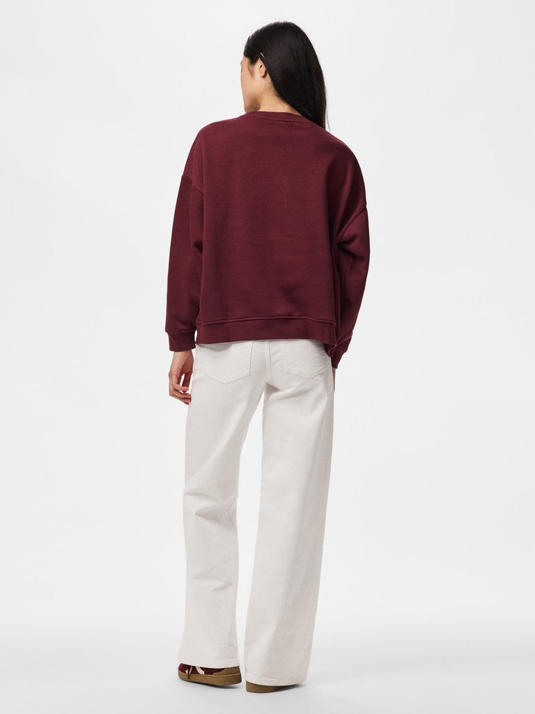 A woman shown from the back wearing a dark burgundy crewneck sweatshirt and off-white wide-leg trousers, standing against a plain white studio background.