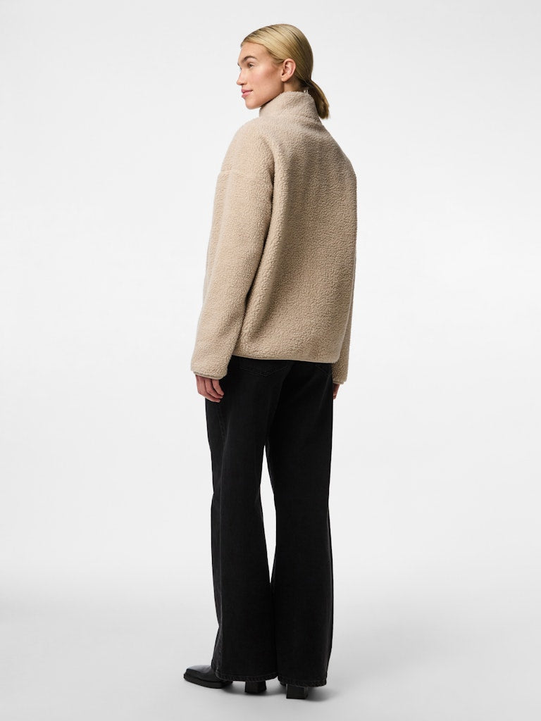 Person wearing a beige sweater and black pants on a white background