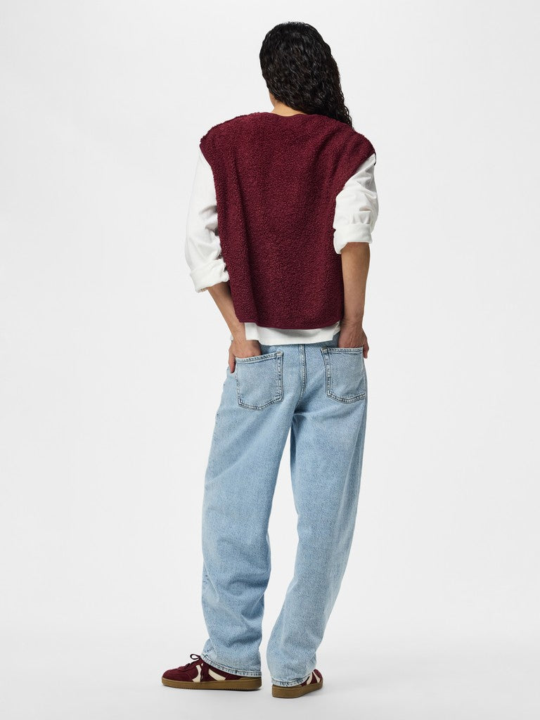 Person wearing a red vest, white shirt, and blue jeans on a white background