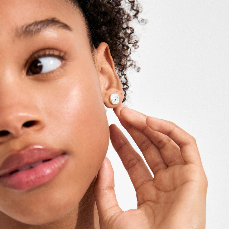 Close-up of a woman wearing a silver earring on a plain background