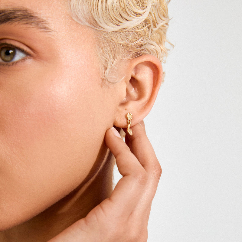 Close-up of a person wearing gold earrings with a neutral background