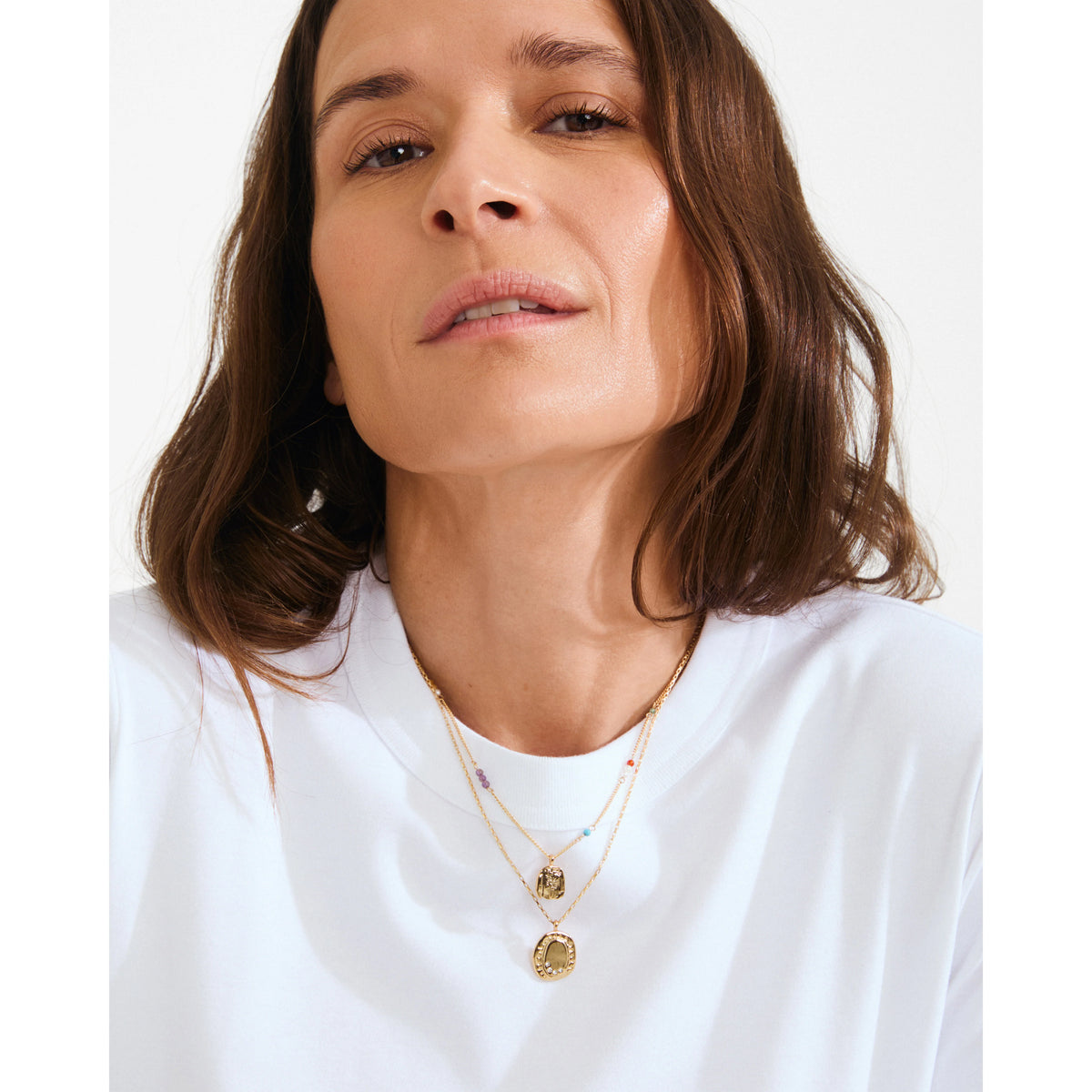 Woman wearing a white shirt and gold necklaces with a plain background