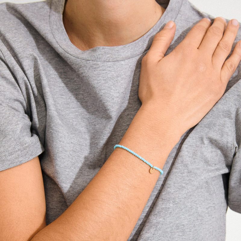 Person wearing a gray t-shirt with a hand on the chest, showing a blue bracelet.