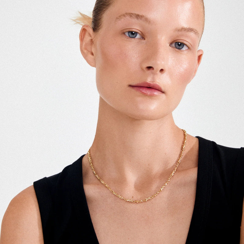 Woman wearing a gold necklace on a plain background
