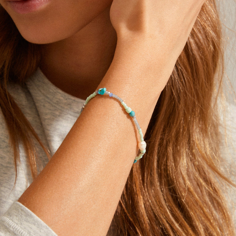 Close-up of a person wearing a bracelet with turquoise beads on a neutral background