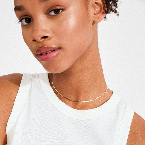 Close-up of a person wearing a gold necklace on a white background