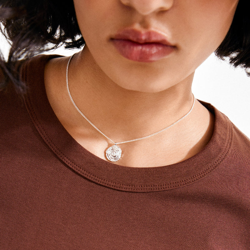 Person wearing a necklace with a circular pendant on a plain background