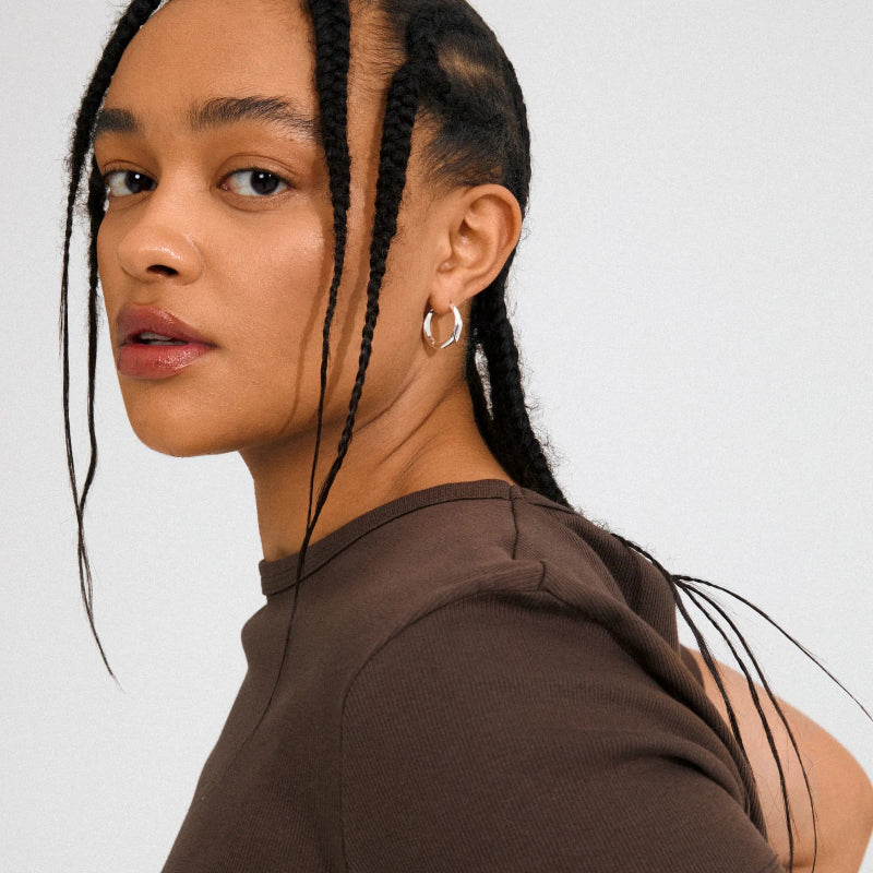 Woman with braided hair wearing a brown top on a white background