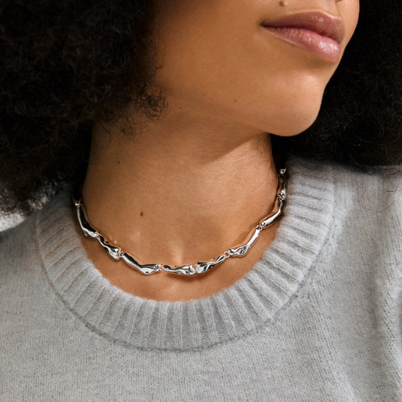 Person wearing a silver chain necklace with a gray sweater