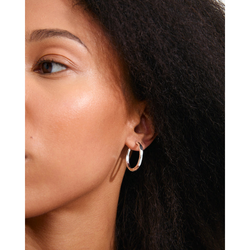 A close-up of a woman's ear wearing a thin, polished silver hoop earring.