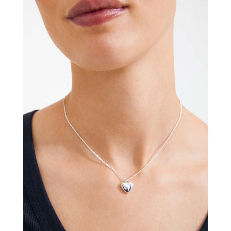Silver heart-shaped necklace on a person against a white background
