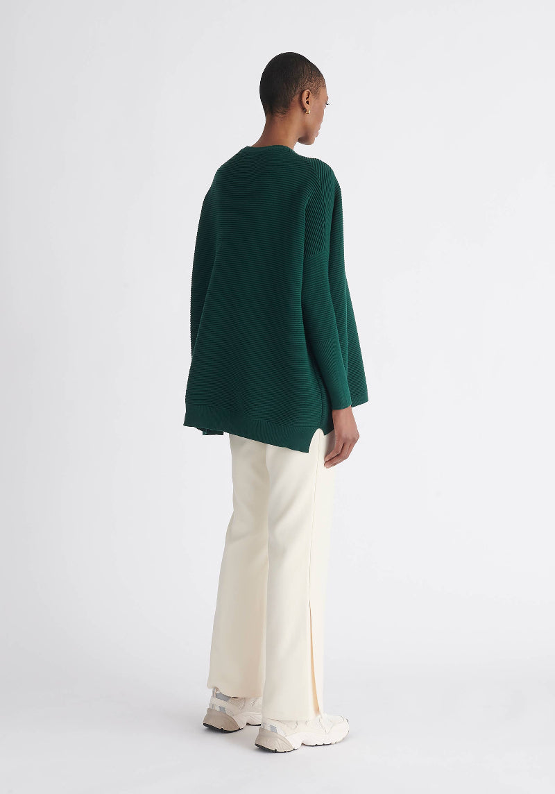 Person wearing a green sweater and white pants on a light gray background