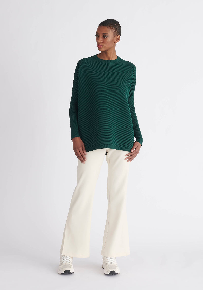 Person wearing a green sweater and white pants on a white background