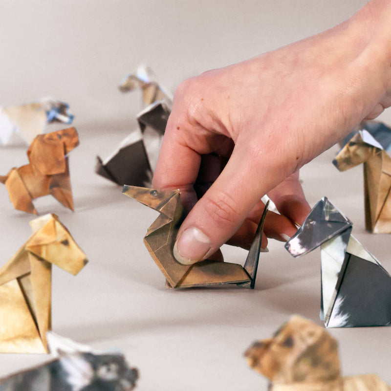 Hand interacting with paper origami animals on a light surface