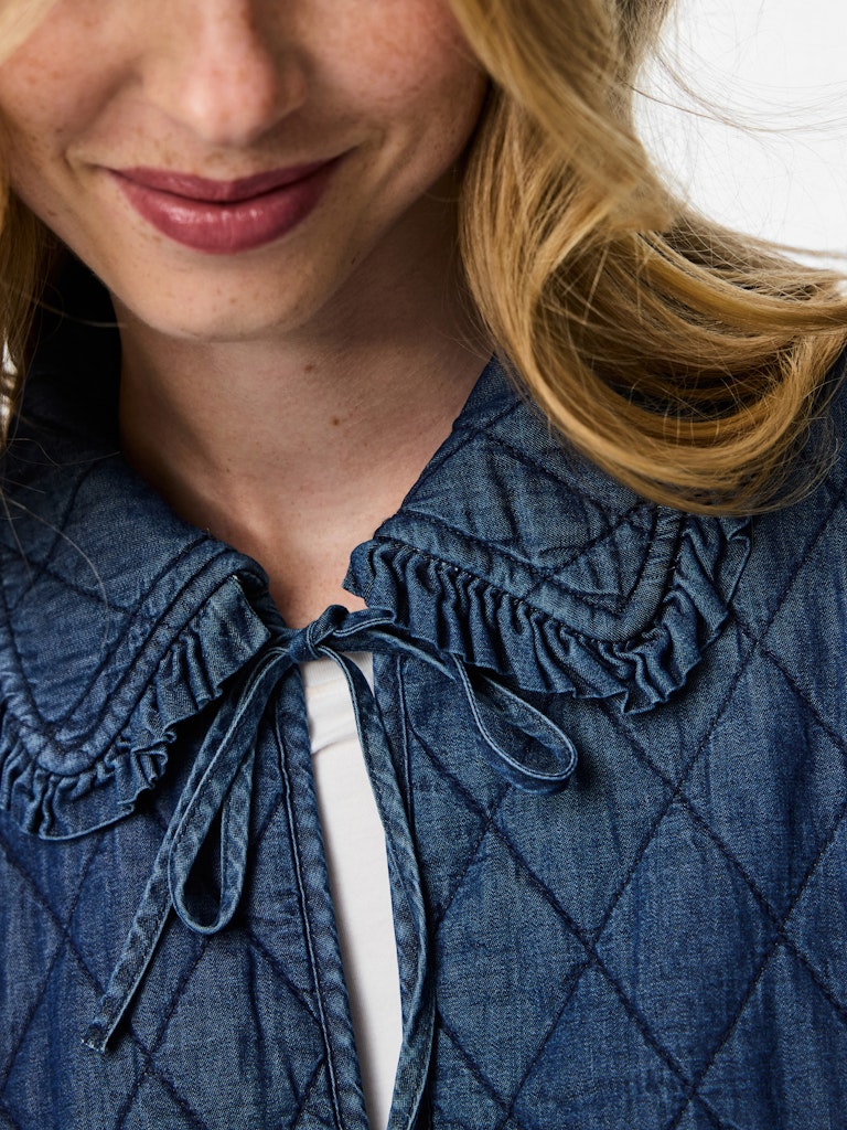 Close-up of a person wearing a blue quilted jacket with a white shirt underneath.