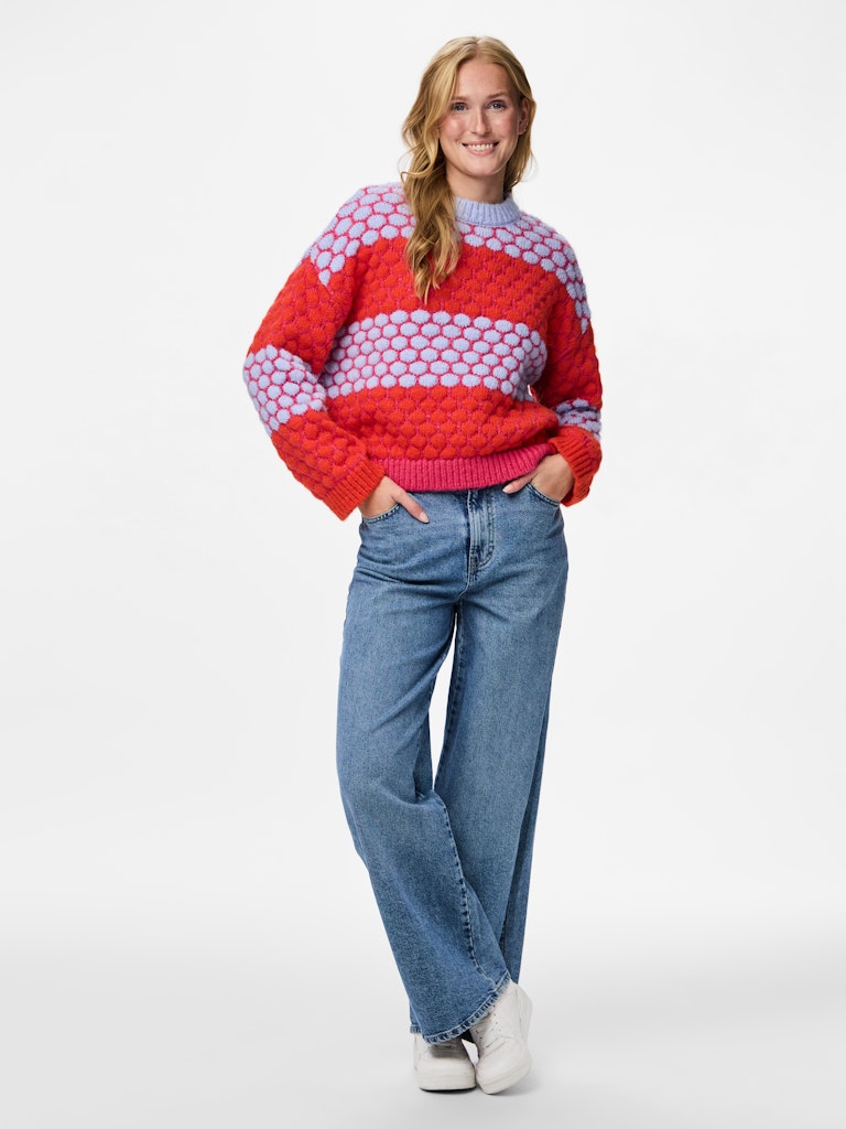 Woman wearing a colourful Pieces Janel Knit Jumper sweater and blue jeans on a white background