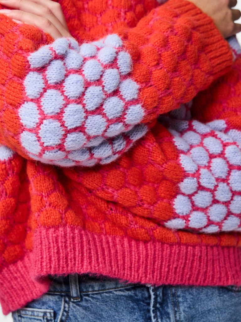 Close-up of a person wearing a red and pink knitted sweater with white patterned sleeves. Pieces Janel Knit Jumper
