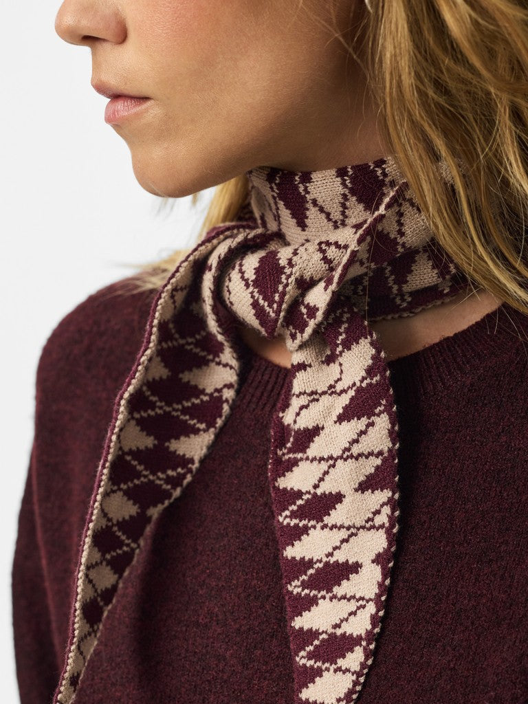 A close-up of a woman wearing a burgundy knit sweater and a matching burgundy and cream patterned scarf tied around her neck.