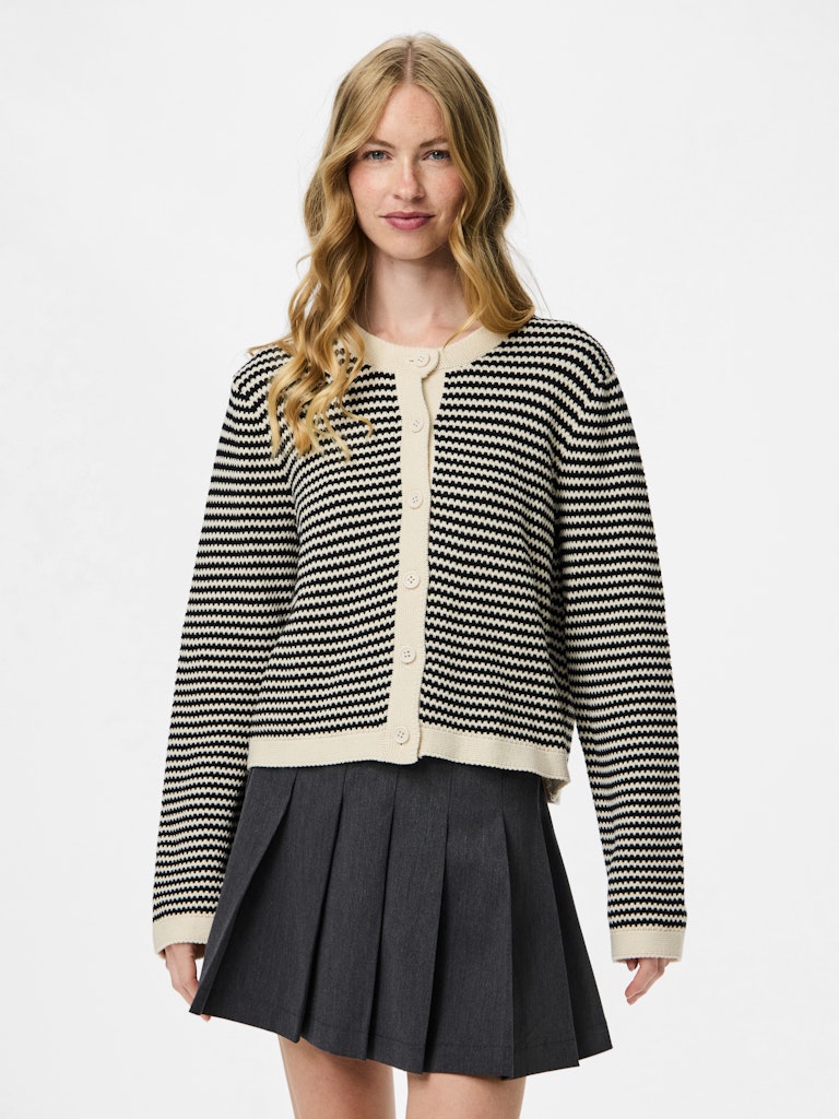 Woman wearing a Pieces Olivera Black & White Striped Cardigan with a beige collar and a black pleated skirt on a light gray background.