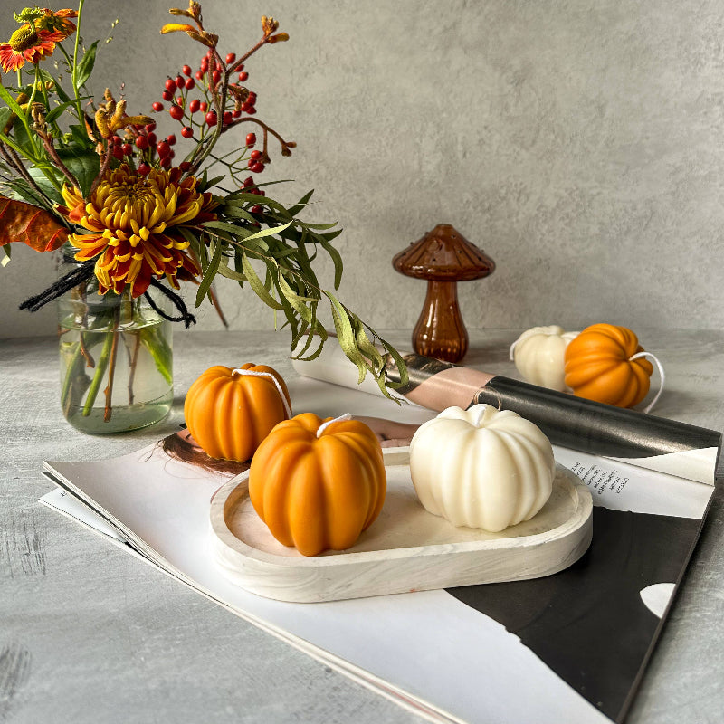 Decorative setting with pumpkins, flowers, and a mushroom on a gray surface.