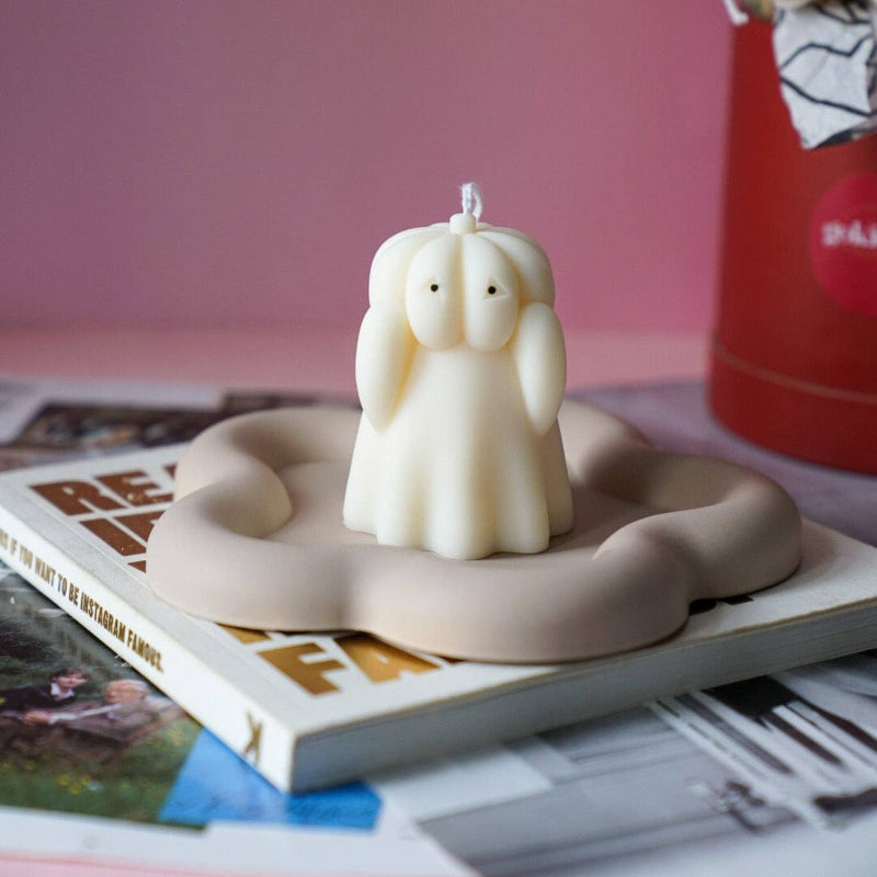 Candle shaped like a angel on a stand with a pink background