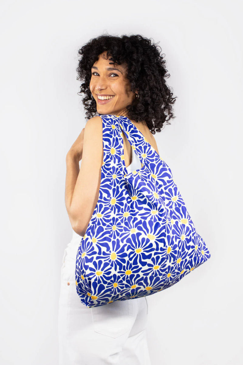 Woman holding a blue floral patterned bag against a white background