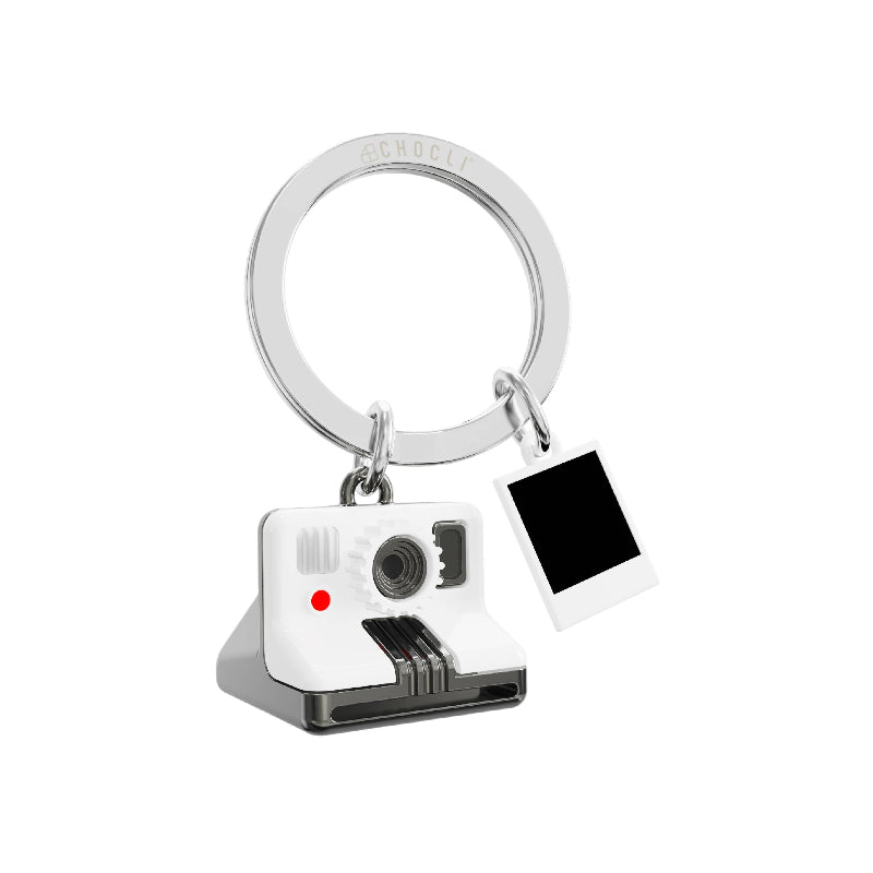 A silver-tone metal keychain featuring a miniature white and gray instant camera charm and a blank white square polaroid-style photo tag, shown on a plain white background.