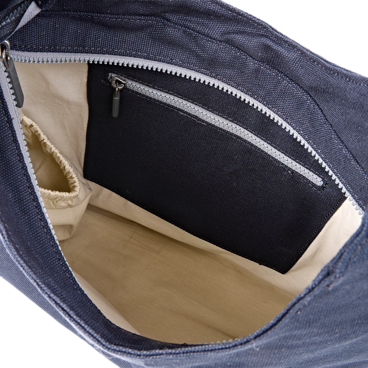 Close-up of the interior of a navy blue canvas bag, showing a beige fabric lining, a zippered pocket, and a side slip pocket.