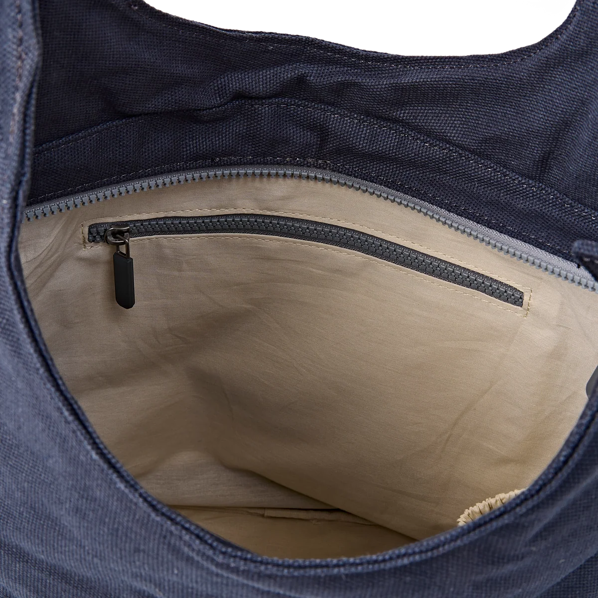 Close-up of the interior of a navy blue fabric bag, showing a beige fabric lining with a zippered pocket and a black zipper pull.
