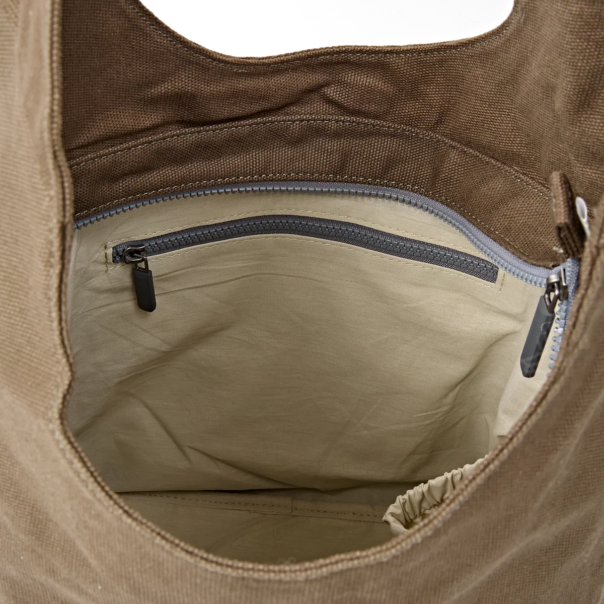 Close-up of the interior of a brown canvas tote bag, showing a beige fabric lining with a gray zipper pocket and dark zipper pulls.