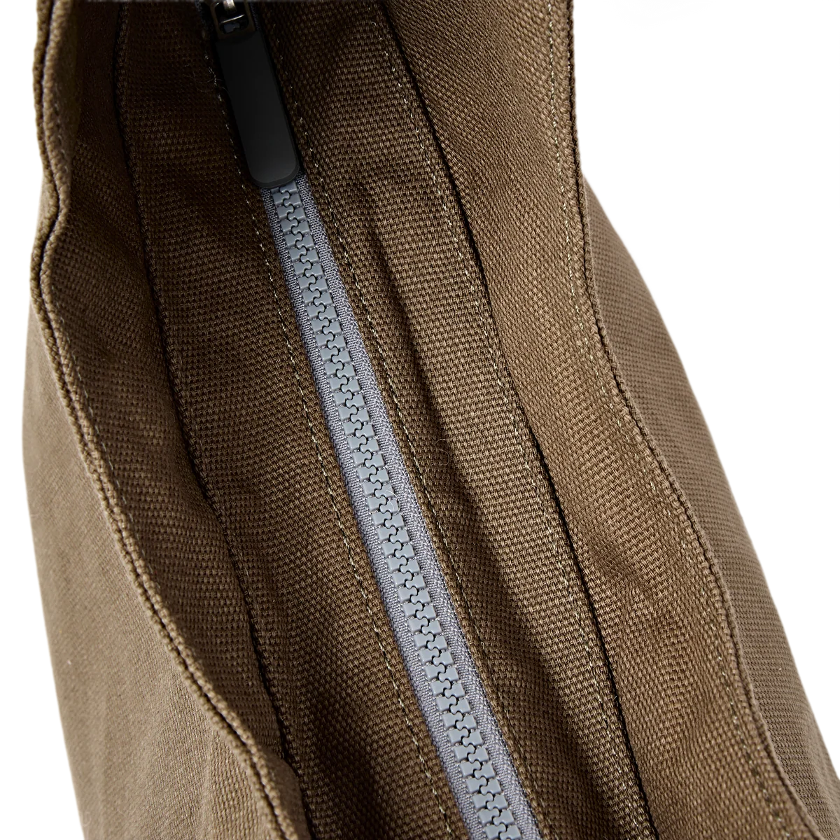 Close-up of a brown canvas bag showing a gray zipper with a black pull tab against a white background.